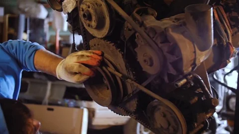 A bearded car mechanic examines the engine of the car suspended on the crane. Video stock 77176294