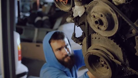 The bearded car mechanic sits and from below screws the bolt into the body of Stock Footage 77176653