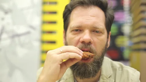 A bearded Caucasian man eats fried chicken wings and nuggets in a fast food cafe Stock Footage 94631577