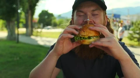 Bearded caucasian man eats meat burger with pleasure, close up Stock Footage 279434757