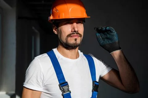 Bearded construction worker in overalls puts on a helmet Stock Photos