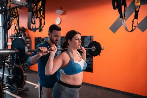 Bearded dark-haired trainer helping plump woman to lift barbell Foto stock
