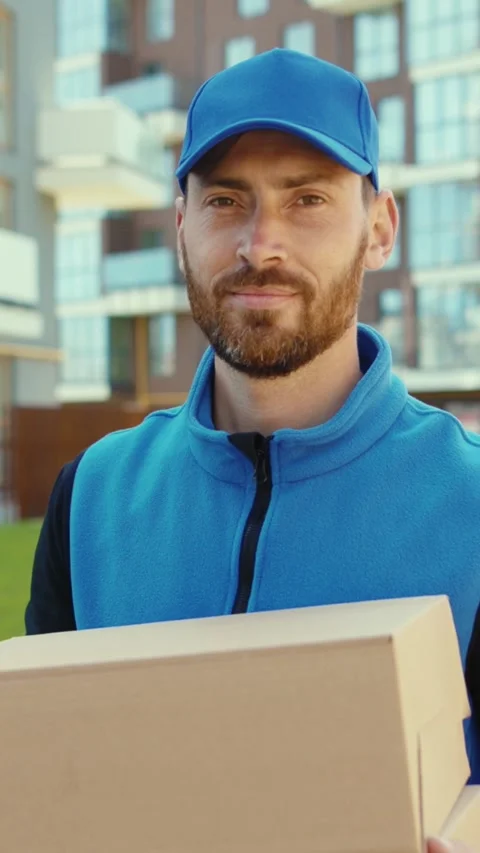 A bearded delivery man in blue confidently carries a box Stock Footage 314961738