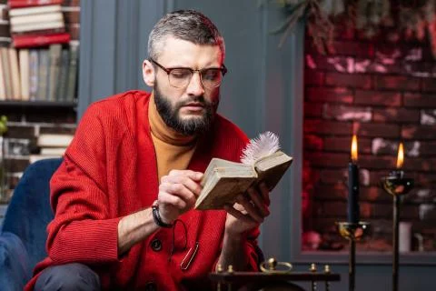 Bearded diviner sitting at the table with candles and enjoying self-education Stock Photos