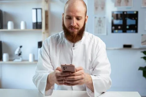Bearded Doctor using smartphone on workplace in clinic. professionalism and.. Stock Photos