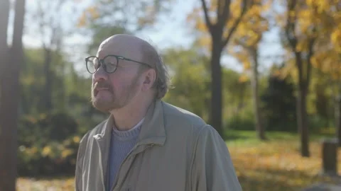 Bearded elderly man with glasses standing in a peaceful autumn setting Stock Footage 297254261