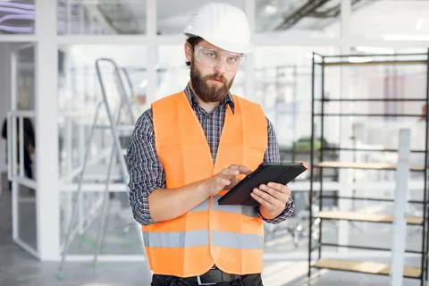 Bearded engineer in helmet and glasses working on tablet Stock Photos