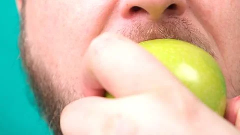 A bearded fat man eats a green apple. Close-up Stock Photos