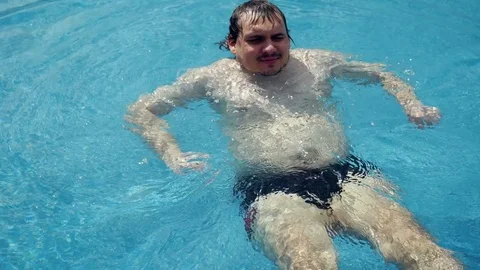 Bearded fat man swims on back along city view swimming pool surrounded Stock Footage 76067197