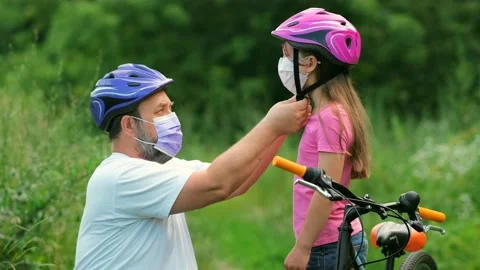 A bearded father puts on a protective Bicycle helmet for his daughter. Stockbeeldmateriaal 134499391