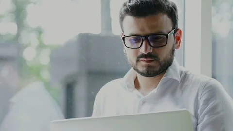 Bearded freelancer with glasses working on the laptop indoor and looking to the Stock Footage 112987612