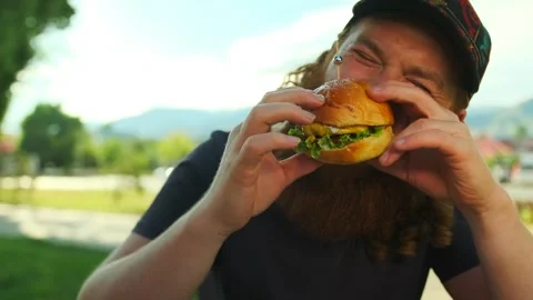 Bearded glutton man eats meat burger with pleasure  in fast food cafe Stock Footage 279434909