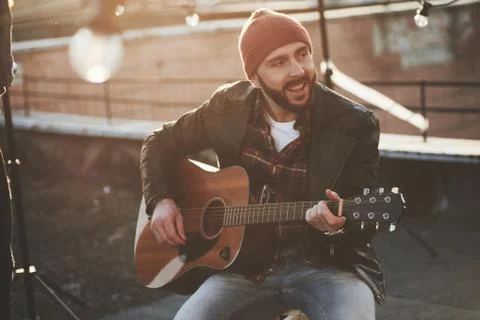Bearded guy in cap playing and singing on the rooftop at nice autumn day Stock Photos