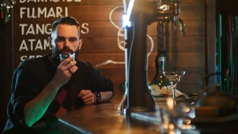Bearded guy drinks a cocktail and communicates with the bartender at the bar Stock Footage 87784021