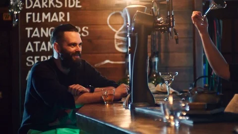 Bearded guy drinks a cocktail and communicates with the bartender at the bar Stock Footage 87784828
