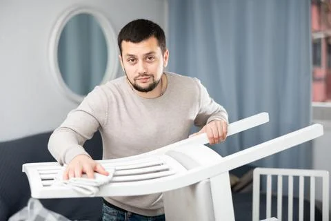 Bearded guy dusting white wooden chair at home Stock Photos