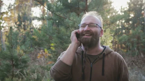 Bearded guy having fun talking on the phone in the woods 库存影片 100675973