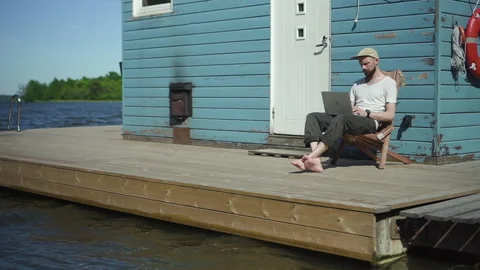 Bearded guy hipster is working with laptop and having nice day at lake pier on Stock Footage 134868422