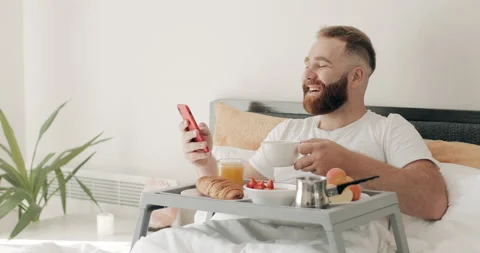 Bearded guy holding coffee cup and reading funny message or joke while lying on Stock Footage 132733577