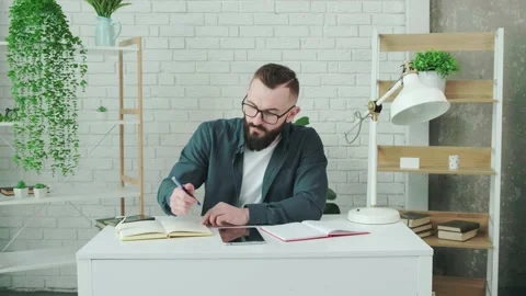 Bearded guy learn online courses using a tablet and write notice in his notebook Stock Footage 155807339