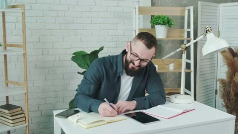 Bearded guy learn online courses using a tablet and write notice in his notebook Stock Footage 158450839