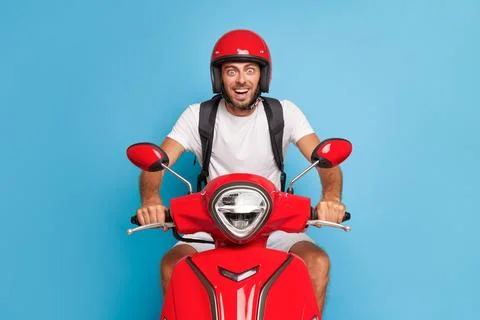 Bearded guy posing on red scooter against blue background in studio, wearing Foto stock