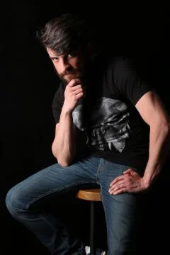 Bearded guy sitting on a bar stool and holding his chin . Close.up. Black Stock Photos