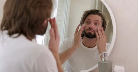 Bearded guy in white shirt applying white mask on face with fingers at home Stock Footage 142528716