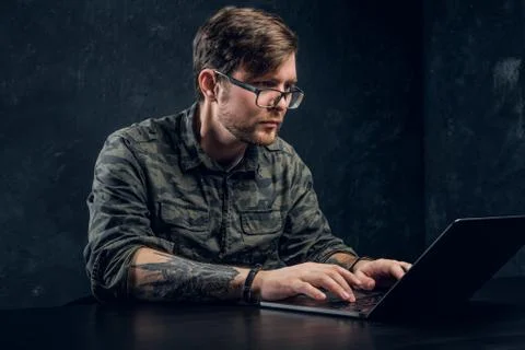 Bearded hacker in glasses makes hacking sitting behind a laptop Stockfoto's