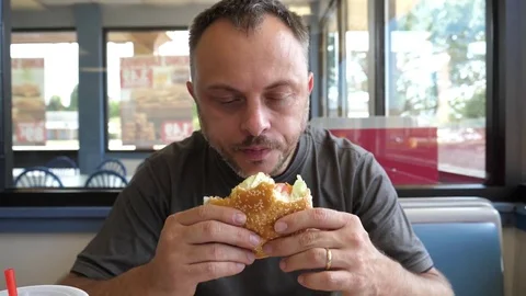 Bearded handsome man eats burger sandwich at the fast food chain restaurant Stock Footage 80745579