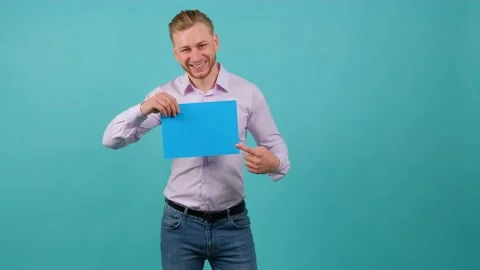 A bearded happy young man points to a blue sheet he holds in his hand. Stock Footage 142097885