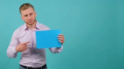 A bearded happy young man points to a blue sheet he holds in his hand. Stock Footage 142098112