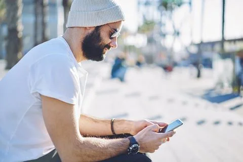 Bearded hipster guy in sunglasses browsing website via mobile technology Stock Photos