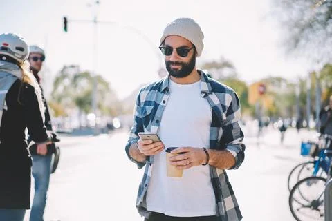 Bearded hipster guy in winter hat browsing content and writing mail message via Stock Photos