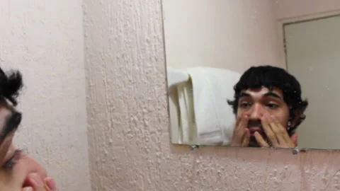 Bearded Hispanic young man looking at his face in the bathroom mirror Video stock 132521251