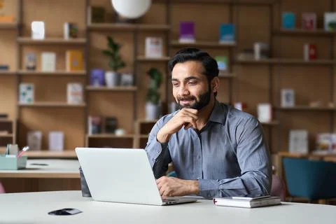Bearded indian business man watching online webinar on laptop computer. Stock Photos