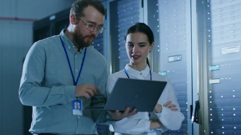 Bearded IT Admin in Glasses with a Laptop Computer and Beautiful Young Technici Stock Footage 100806989