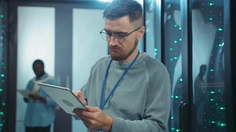 Bearded IT engineer browsing data on digital tablet in server room. Euphoric Stock Footage 119787131