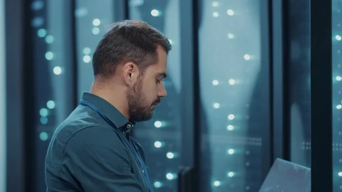 Bearded IT expert examining server cabinet with notebook, doing web hosting Stock Footage 121224109