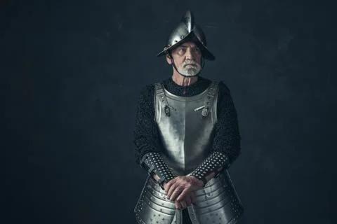 Bearded knight standing with sword in front of gray wall. Stock Photos