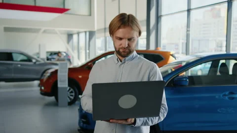 Bearded male manager with laptops on the background of a car dealership Stock Footage 203769368