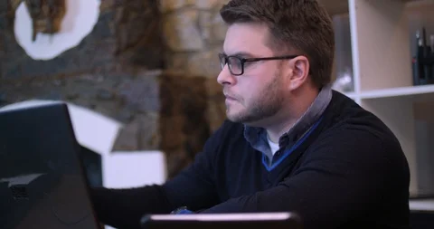 A bearded man is actively working and trying to talk on the phone. Attractive Stock Footage 87322762