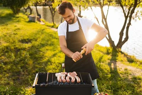 Bearded man adding spices to meat on grill Stock Photos