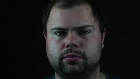 A bearded man against a dark background looking at the camera and licks his lips Stock Footage 130222329