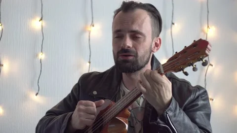 A bearded man are playing the 6-strings ukulele and sings Stock Footage 170087452