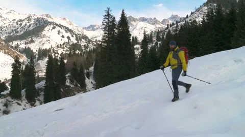 A bearded man with a backpack descends a snowy slope in the mountains Stock Footage 233987326