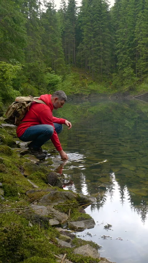 A bearded man with a backpack drinks water from a clean lake Stock Footage 336432653