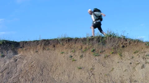 Bearded man with backpack jumping off a cliff Stock Footage 65483230