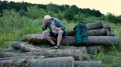 A bearded man with a backpack sitting on logs and washes. Stock Footage 65484034