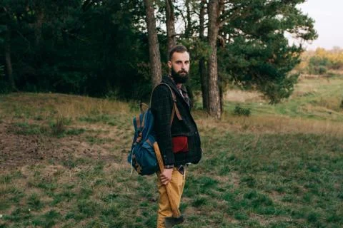 Bearded man with a backpack standing in the forest. Travel concept Stock Photos